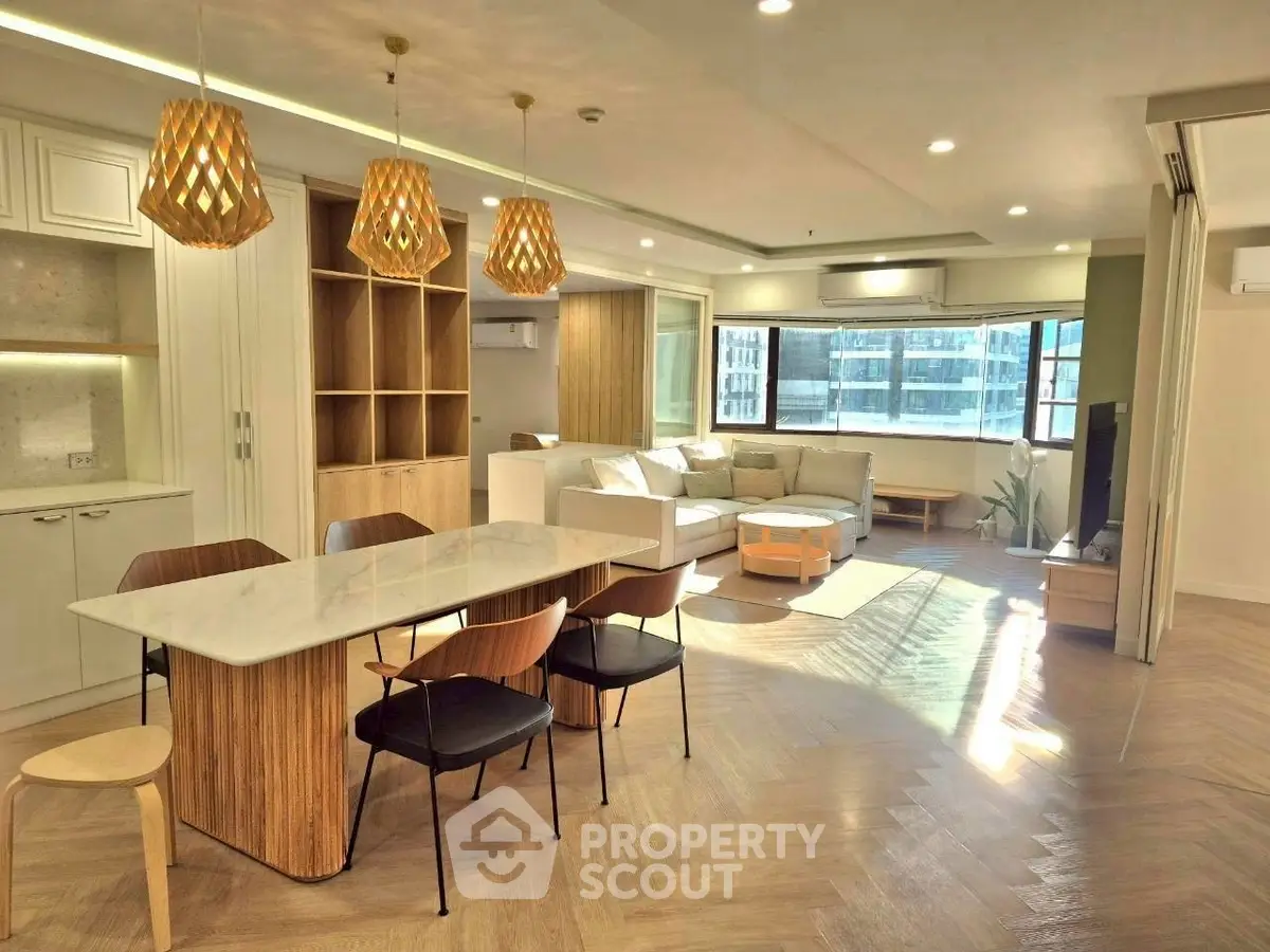 Spacious modern living room with open kitchen and stylish lighting in a sunlit apartment.