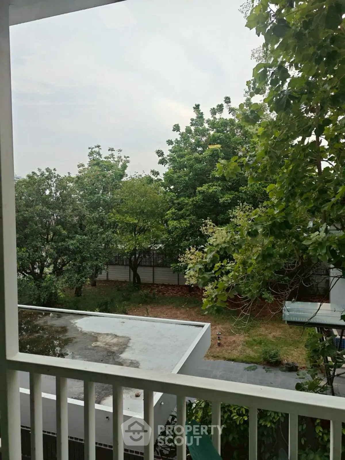 Serene garden view from a balcony with lush greenery and modern architecture.