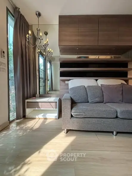 Modern living room with elegant chandelier and cozy sofa, featuring wooden accents and large windows for natural light.