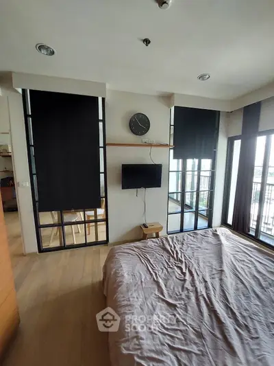 Modern bedroom with large windows and balcony access, featuring sleek design and natural light.