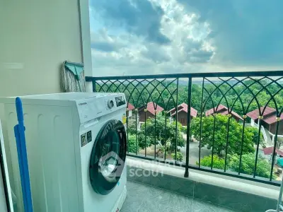 Scenic balcony view with washing machine overlooking lush greenery and rooftops.