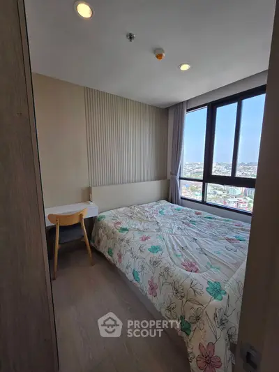 Cozy bedroom with large window offering stunning city views, featuring a stylish bed and a modern desk.