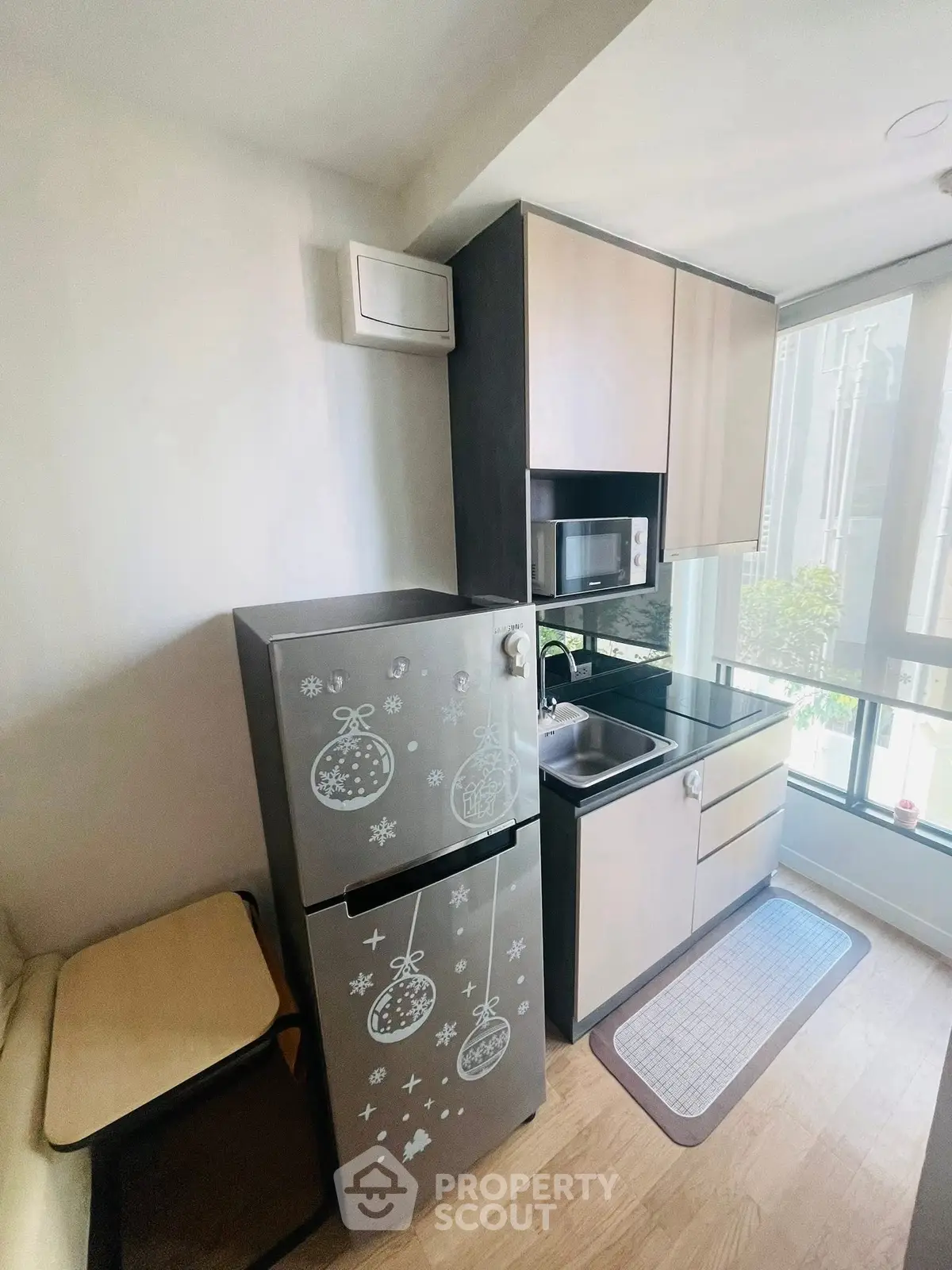 Compact modern kitchen with fridge, microwave, and large window for natural light.