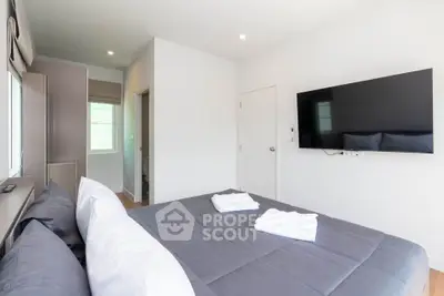 Modern bedroom with wall-mounted TV and cozy bedding in bright apartment
