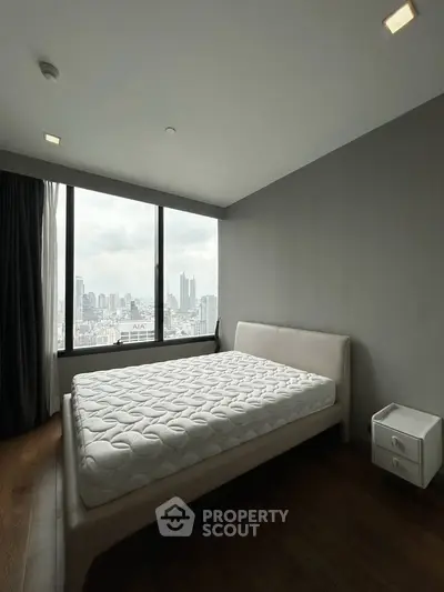 Spacious bedroom with city view and modern furnishings in high-rise apartment.