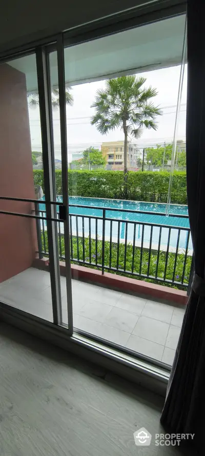 Modern apartment with pool view from balcony, featuring large sliding glass doors and lush greenery.