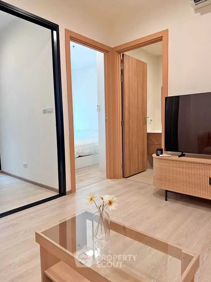 Modern living room with glass coffee table and TV, leading to a cozy bedroom