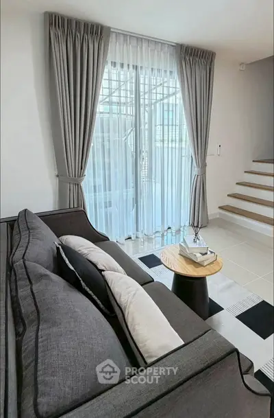 Modern living room with elegant gray sofa and stylish decor, featuring large windows and natural light.