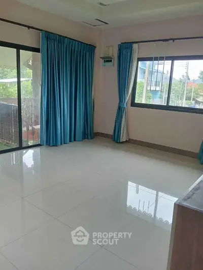 Spacious living room with large windows and blue curtains, offering abundant natural light and garden view.