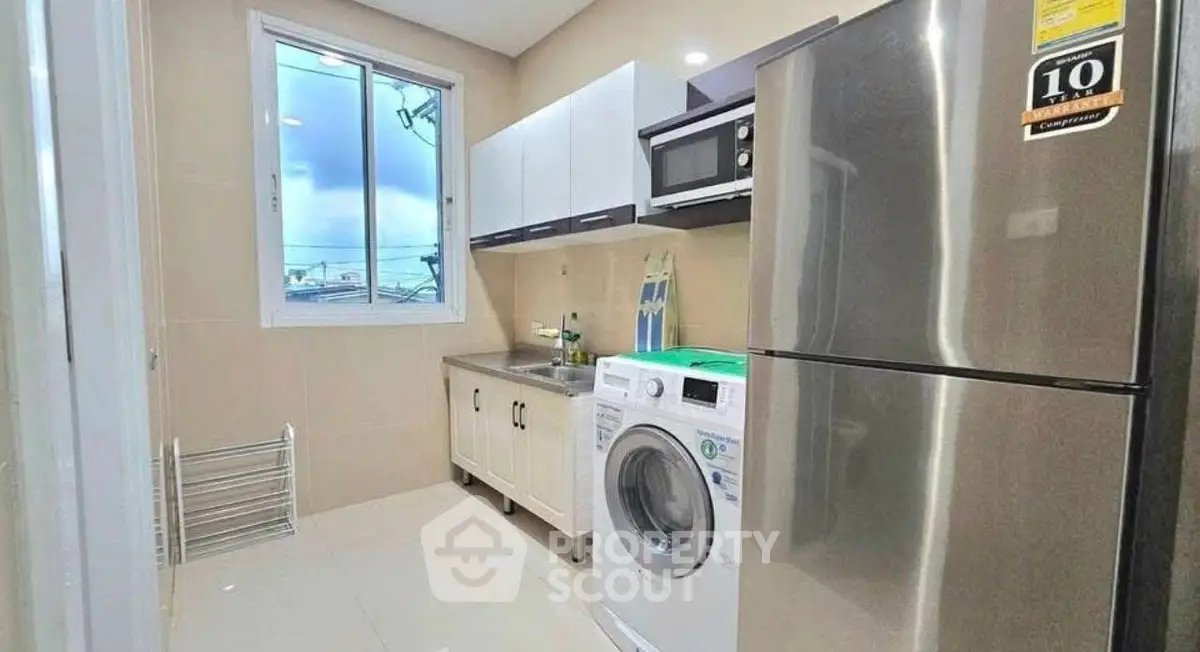 Modern kitchen with stainless steel fridge and washing machine, bright window view.