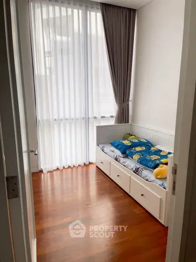 Cozy small bedroom with wooden flooring and large window for natural light.