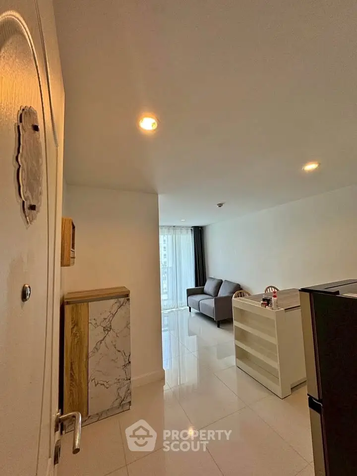Modern apartment entrance leading to a bright living room with sleek furnishings and glossy floors.