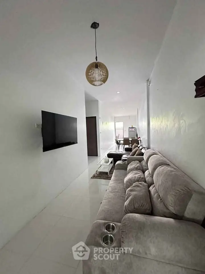 Modern living room with plush gray sofa and wall-mounted TV, leading to dining area.