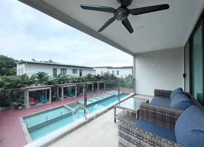 Luxurious balcony overlooking a pristine pool with modern outdoor furniture and ceiling fan.