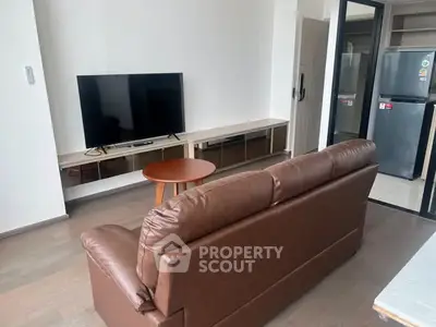 Modern living room with sleek brown sofa and flat-screen TV, adjacent to a compact kitchen area.