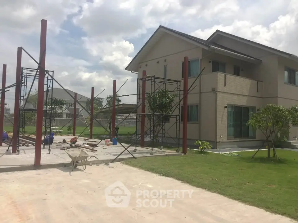 Modern two-story house with construction in progress, spacious lawn, and clear sky.