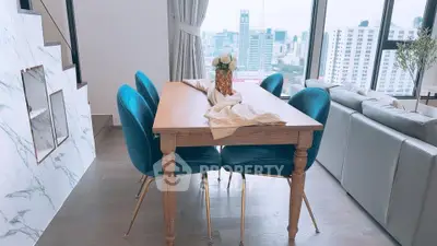 Stylish dining area with city view, featuring elegant wooden table and plush blue chairs in modern apartment.