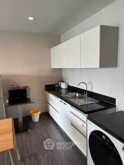 Modern kitchen with sleek cabinets and appliances, featuring a washing machine and microwave.
