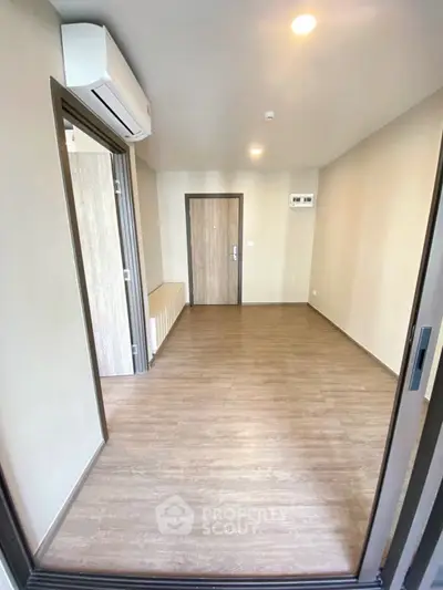 Spacious empty room with wooden flooring and air conditioning, perfect for customization.