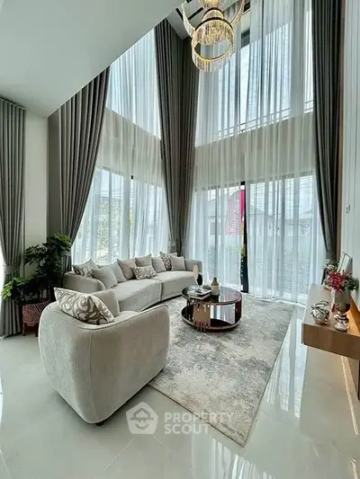 Luxurious living room with high ceilings, elegant chandelier, and large windows for natural light.
