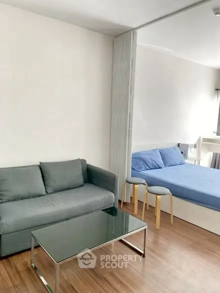 Modern studio apartment with sleek furniture and wooden flooring, featuring a cozy living area and bedroom.