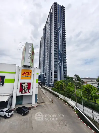 Modern high-rise building next to commercial area with ample parking space and lush greenery.