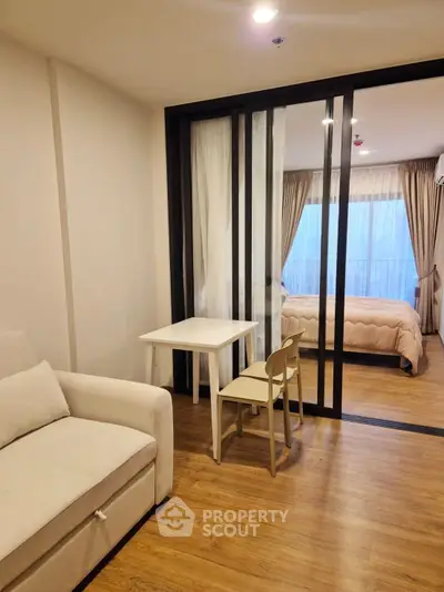 Modern apartment interior with cozy living room and bedroom separated by sliding glass doors, featuring wooden flooring.