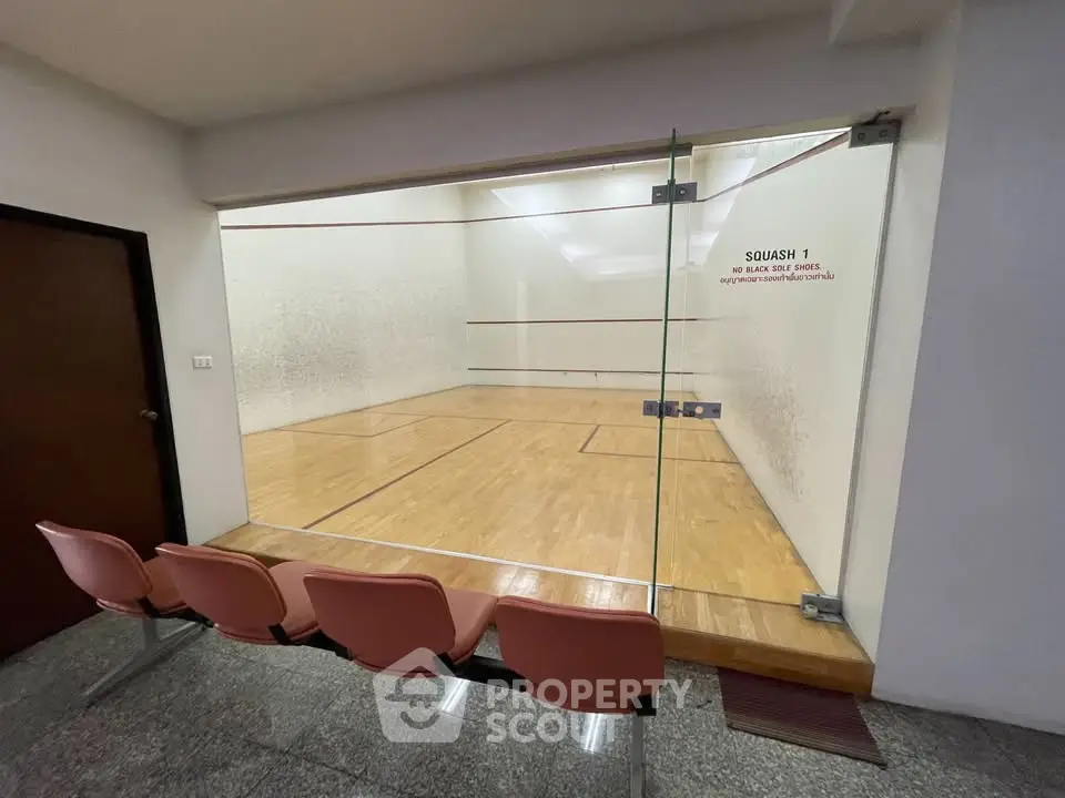 Modern squash court with glass wall and seating area in luxury residential building.