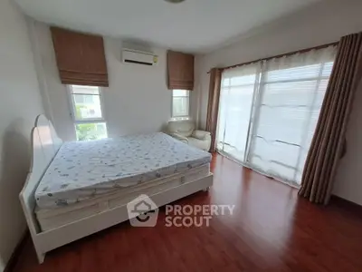 Spacious bedroom with large windows and elegant curtains, featuring a comfortable bed and wooden flooring.