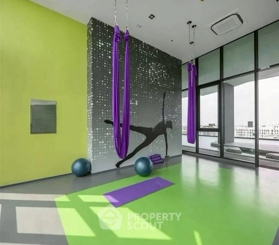 Modern gym with aerial yoga setup and city view, perfect for fitness enthusiasts.
