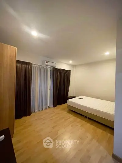 Spacious bedroom with wooden flooring and large window for natural light