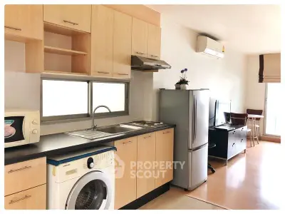 Modern kitchen with wooden cabinets, washing machine, and stainless steel fridge in bright apartment.
