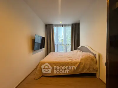 Cozy bedroom with modern decor and wall-mounted TV, featuring natural light from large window.