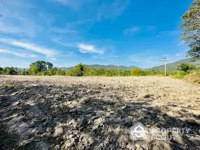 Expansive barren land ready for development with a backdrop of lush mountains under a clear blue sky, ideal for a custom real estate project.