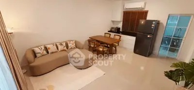 Modern living room with cozy sofa, dining area, and sleek kitchen featuring stainless steel fridge.