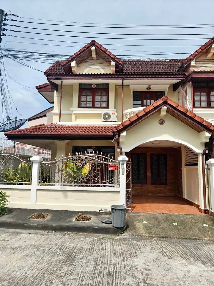 Charming two-story house with red-tiled roof and gated entrance in a serene neighborhood.