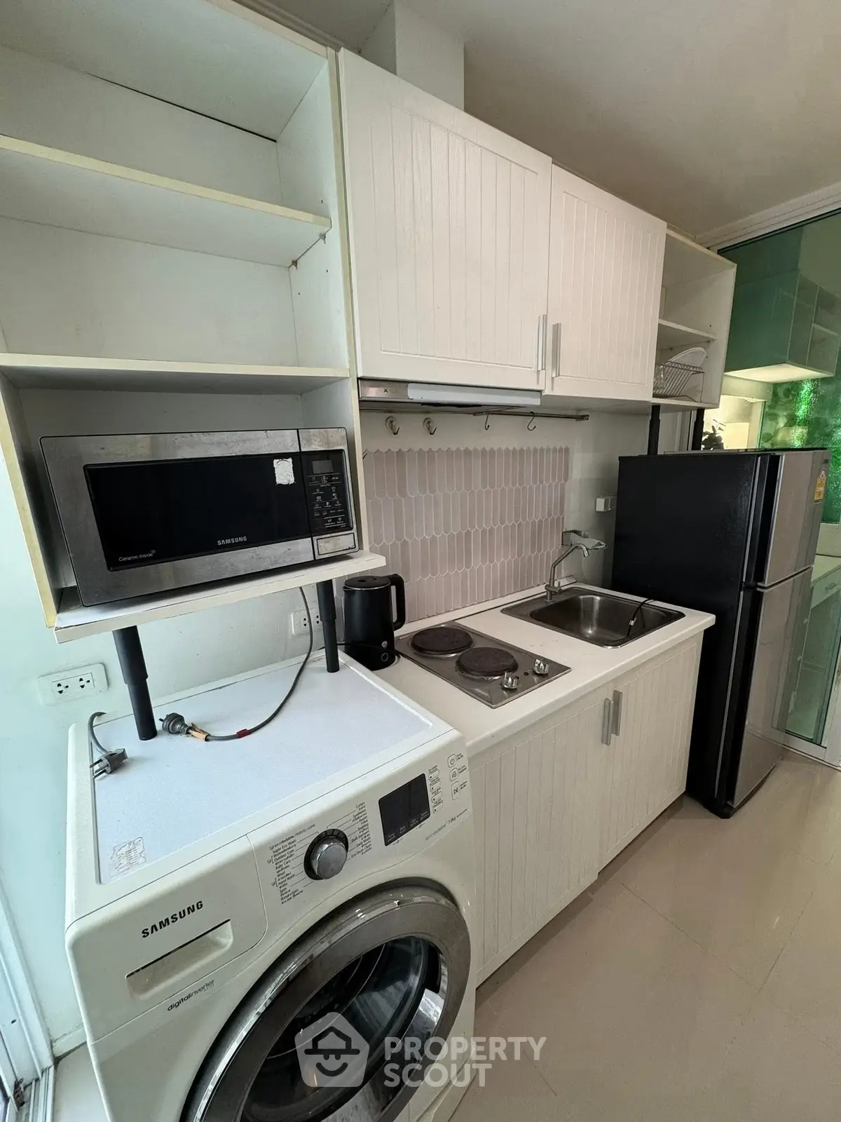 Compact kitchen with modern appliances including washing machine, microwave, and fridge in a sleek white design.