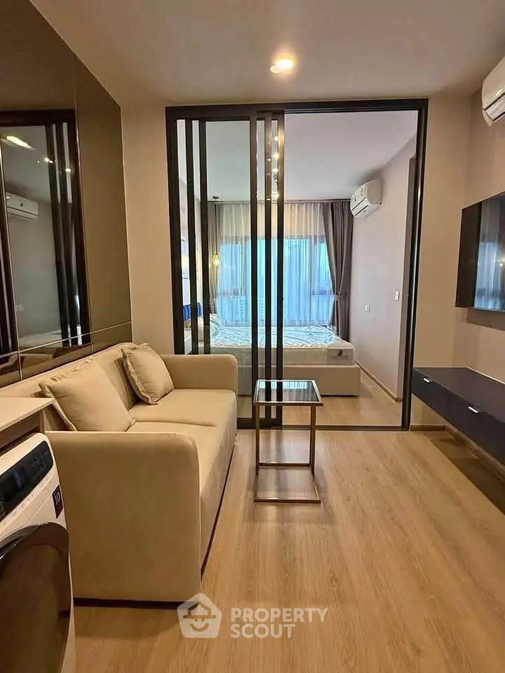 Modern apartment with cozy living room and bedroom separated by glass doors, featuring stylish decor and wooden flooring.