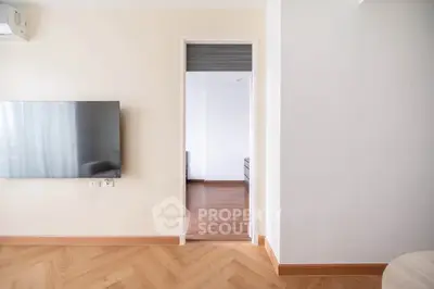 Modern interior with wall-mounted TV and wooden flooring, leading to a bright room.
