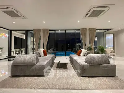 Luxurious modern living room with pool view, featuring elegant gray sofas and floor-to-ceiling windows.