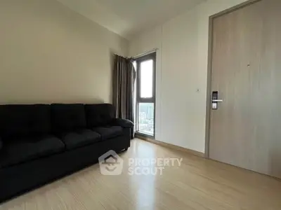 Modern living room with black sofa and city view from window, featuring sleek wooden flooring.
