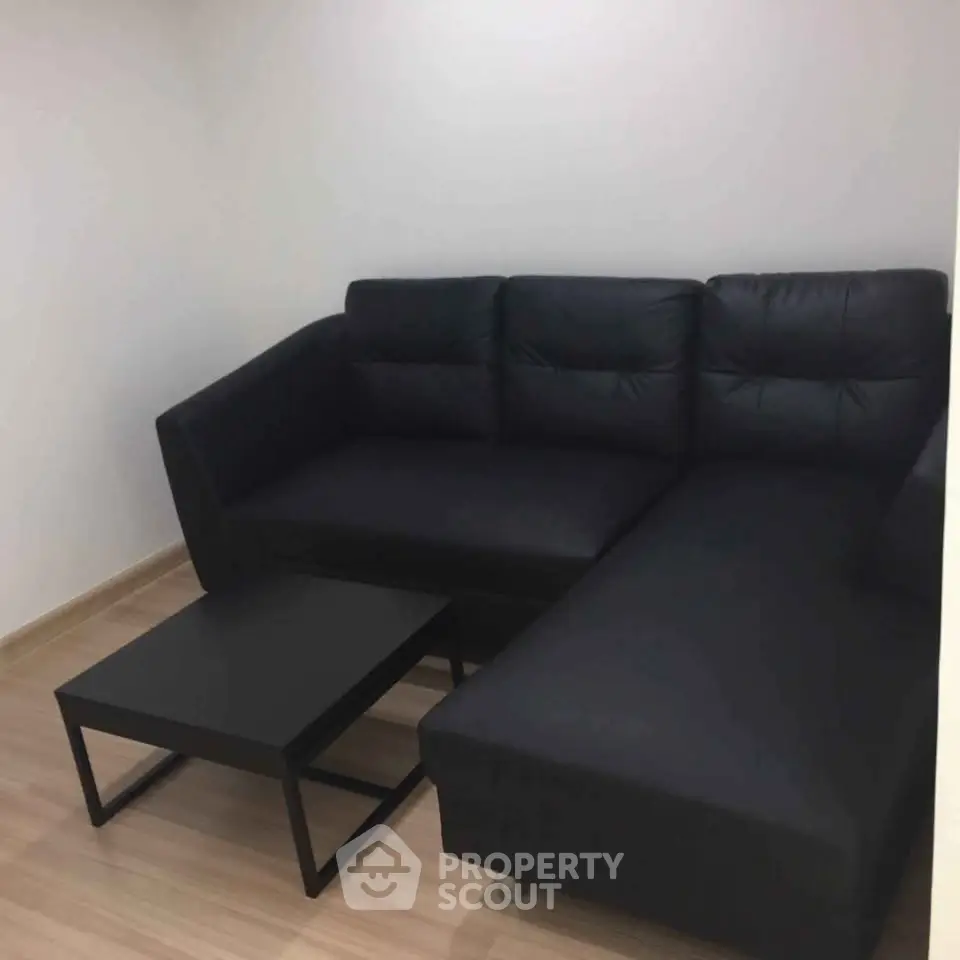 Modern living room with sleek black sectional sofa and minimalist coffee table on wooden flooring.