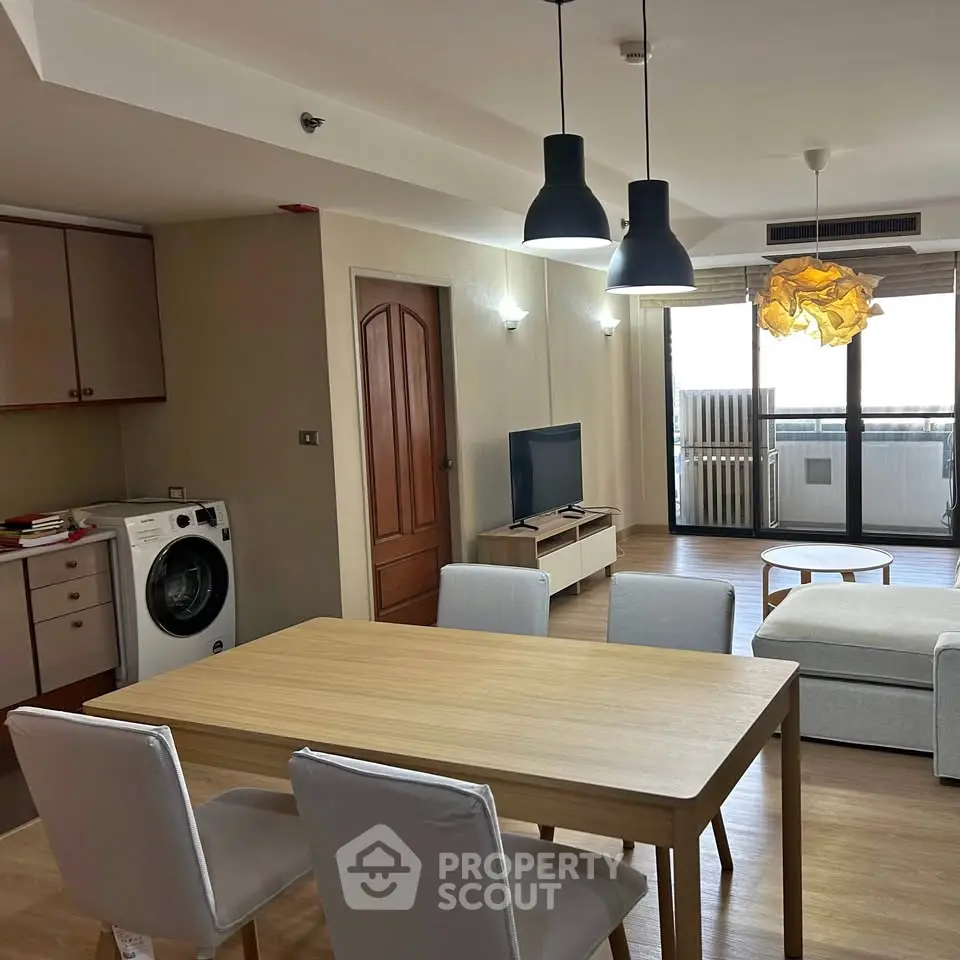 Modern living room with dining area and washing machine, featuring stylish lighting and balcony access.