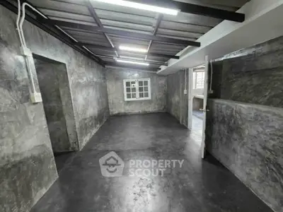 Industrial-style room with concrete walls and floors, featuring a window and open door for natural light.