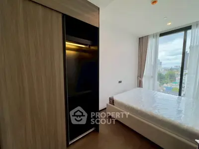 Modern bedroom with large window and city view, featuring sleek wardrobe and comfortable bed.