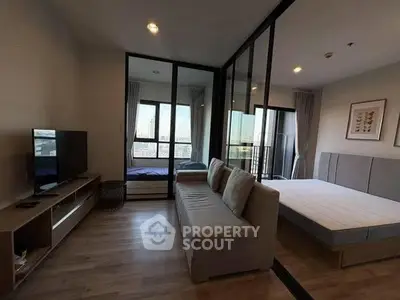 Modern studio apartment with glass partition, cozy living area, and large windows for natural light.