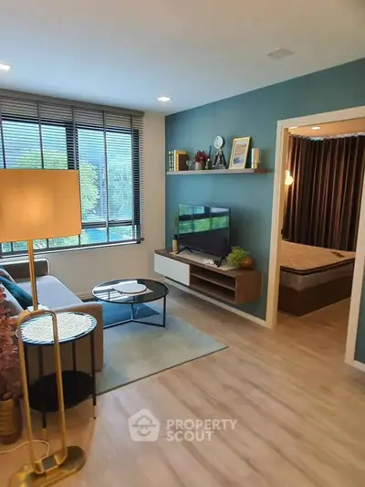 Modern living room with stylish decor and large window offering natural light, adjacent to a cozy bedroom.