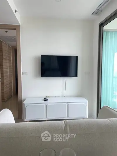 Modern living room with wall-mounted TV and sleek white cabinet in a bright apartment.