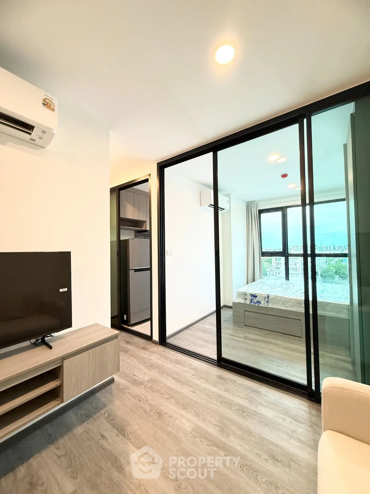 Modern apartment with glass sliding doors and city view, featuring a cozy living area and bedroom.