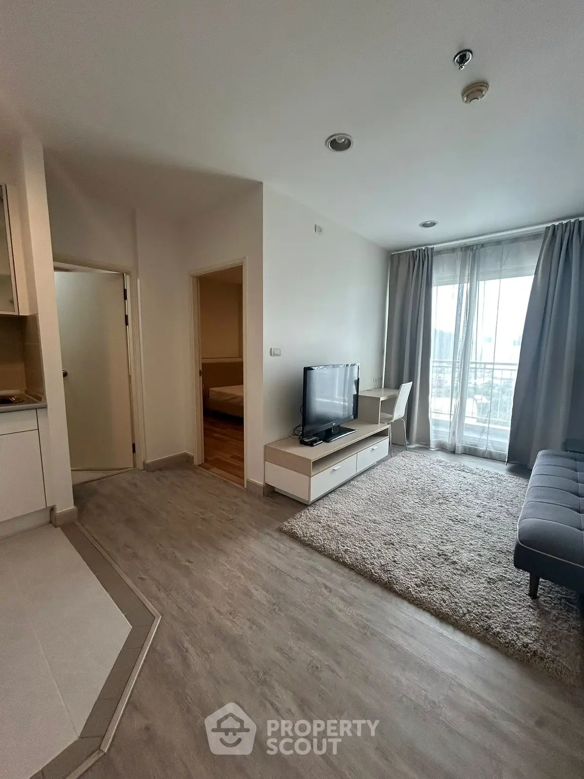 Modern living room with sleek flooring and natural light, featuring a cozy TV area and balcony access.